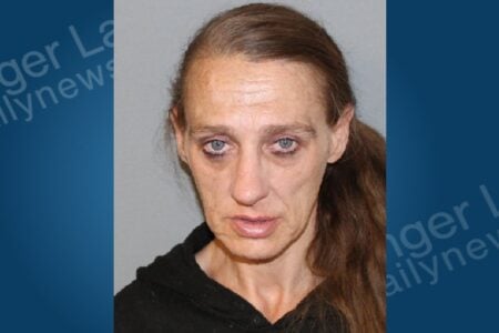 Mugshot of a woman with long brown hair, blue eyes, and a serious expression against a plain background.