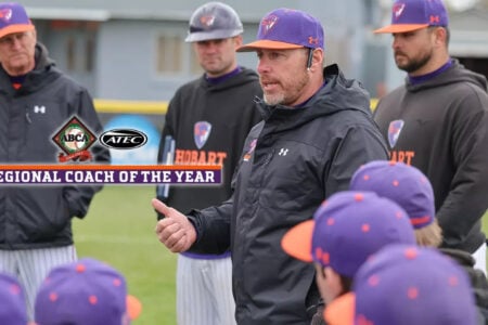 Hobart baseball coach in purple and orange cap speaks to players on a field, recognized as Regional Coach of the Year.