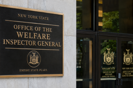 Bronze plaque for the New York State Office of the Welfare Inspector General on a building facade with glass doors.