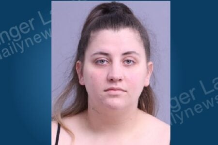 Mugshot of a woman with light brown hair pulled back, light eyes, and a black top, against a plain gray background.