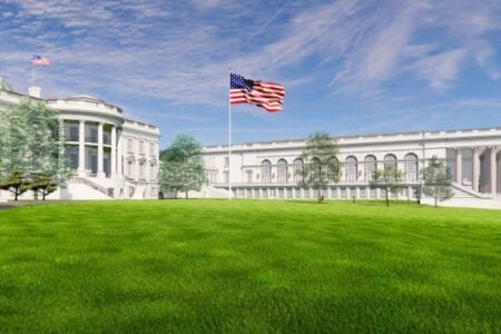 The White House, with a large American flag flying over a green lawn under a blue sky.