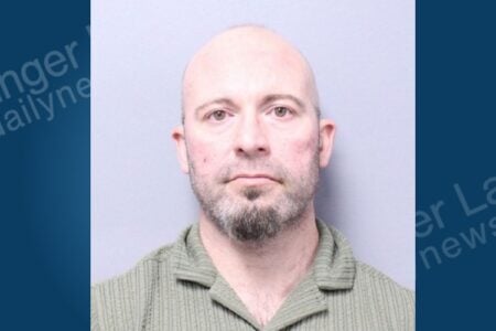 Bald man with a goatee and green striped shirt stares straight ahead in a police booking photo.