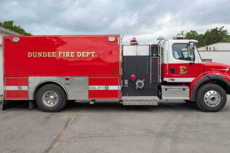 Dundee Fire Department's red and white fire truck parked outside a building, with a man looking towards it.