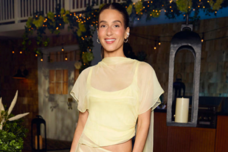 Smiling woman in sheer yellow top at an outdoor evening event with string lights and greenery.