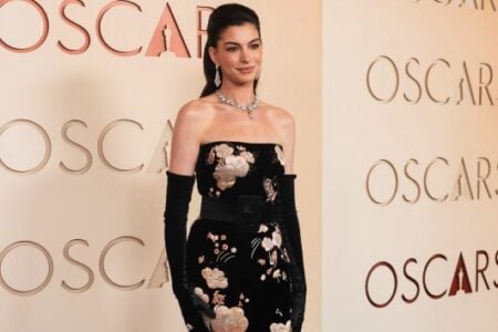 Anne Hathaway poses in a black floral strapless dress and long gloves at an Oscars event.