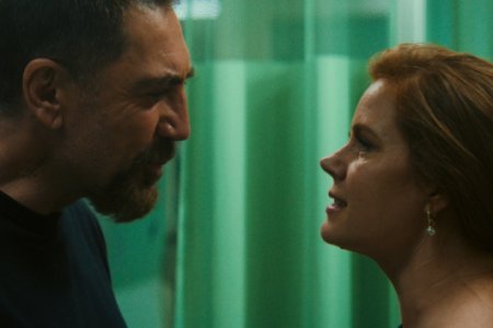 Bearded man and red-haired woman in close, intense discussion against a textured green background.