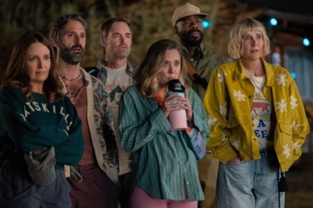 Six adults look with wide-eyed, concerned expressions outdoors at night, surrounded by blue string lights.