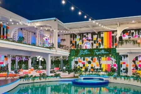 Brightly lit, multi-level outdoor resort set with a pool, vibrant decor, and "Better Together" neon sign at night.
