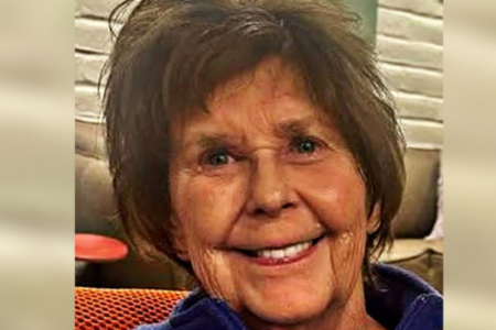 Older woman with short reddish-brown hair, blue eyes, and a warm smile poses for a headshot indoors.