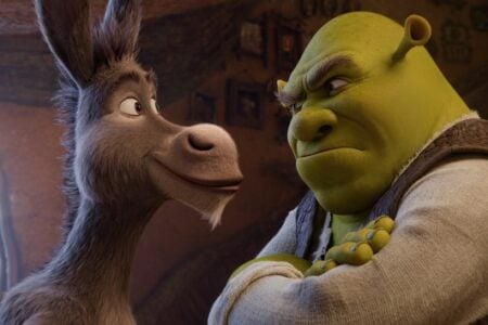 Shrek, the green ogre, scowls with crossed arms at a smiling gray donkey, Donkey, indoors.