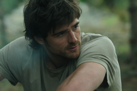 Actor Jacob Elordi, with dark hair and short beard, looks pensively to his right in an outdoor setting.
