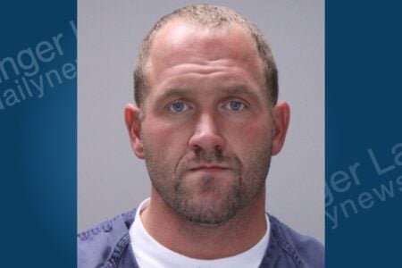 Mugshot of a man with blue eyes, short brown hair, and a beard, wearing a blue shirt, looking forward.