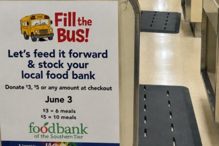 A white "Fill the Bus!" sign featuring a cartoon school bus promotes donations for the Foodbank of the Southern Tier at a checkout counter.