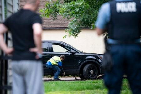 Person in a safety vest works on a black SUV's tire with a jack, observed by a police officer.