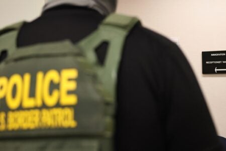 Back of a U.S. Border Patrol officer in an immigration court hallway with a sign pointing to the waiting room.