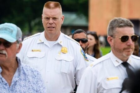 Chief Jim Carroll, in a white police uniform, stands attentively among a crowd outdoors.