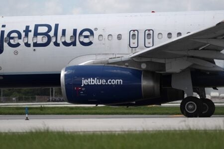 A JetBlue airplane on an airport tarmac, showing its fuselage, engine, and wing.