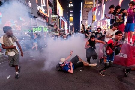 Amid a cloud of smoke in Times Square, people run and react, with one person on the ground and others filming.