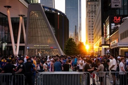 Large crowd in sports attire gathers outside Penn Station, New York City (LIRR/Subway), at sunset with police and barriers.