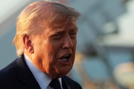 Donald Trump speaks outdoors, his face and signature blond hair glowing in golden hour sunlight.