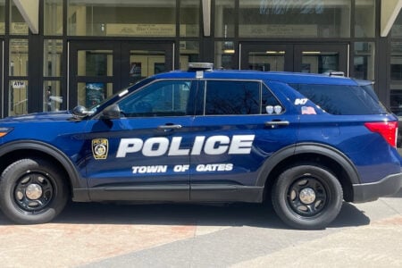 A dark blue Town of Gates police SUV is parked in front of the Blue Cross Arena War Memorial.