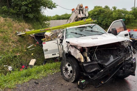 Heavily damaged white utility truck off the road at an accident scene with a NY State Police car.