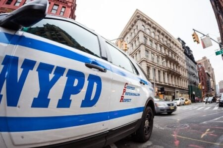 NYPD patrol car on a bustling New York City street (E 18 St) with historic architecture and traffic.