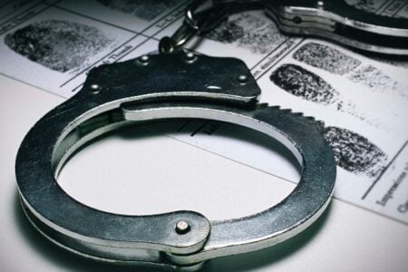 Close-up of silver handcuffs resting on a white document with black fingerprints.