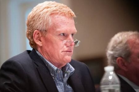 Alex Murdaugh, with reddish-blond hair, looks intently to the side with glasses on his nose, seated in a hearing room.