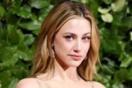 Lili Reinhart with blonde hair and light eyes gazes forward against a green leafy backdrop.