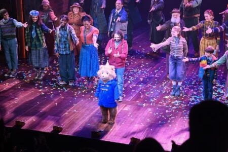 Paddington Bear and cast taking a curtain call on a confetti-covered theater stage.
