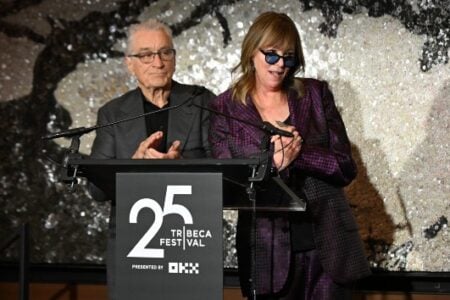 Robert De Niro applauds while Jane Rosenthal speaks into a microphone at the Tribeca Festival.