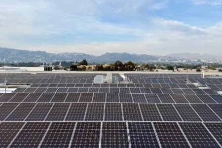 Extensive rooftop solar panel array with a distant city and hills under a partly cloudy sky.