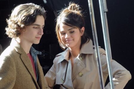 Timothée Chalamet and a smiling Selena Gomez stand together on a sunny outdoor film set.
