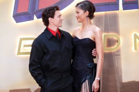 Tom Holland and Zendaya smile, gazing at each other, against a movie premiere backdrop.