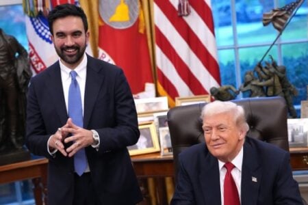 Kash Patel stands smiling next to a seated, smiling Donald Trump in the Oval Office.