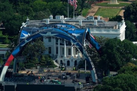 Crew setting up a large stage with patriotic arches on the White House lawn.