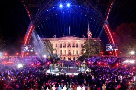 A mixed martial arts cage match takes place before a large crowd at night, with the White House lit up in the background.