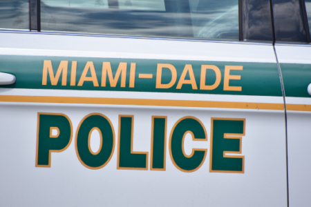 Side of a white Miami-Dade Police patrol car, featuring its green and orange agency name.
