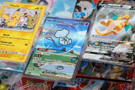 Three Pokemon trading cards, including Pikachu & Mimikyu, Mew ex, and Dragonite V, displayed on a surface.
