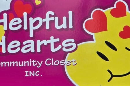 Bright magenta sign with white text for Helpful Hearts Community Closet INC., featuring red and yellow hearts and a smiling emoji.