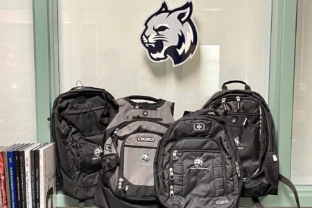 Jasper-Troupsburg branded backpacks, a vest, and a wildcat logo displayed indoors with school yearbooks.