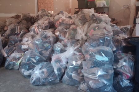 Piles of clear plastic bags filled with shoes are stacked high across the concrete floor of a storage room.