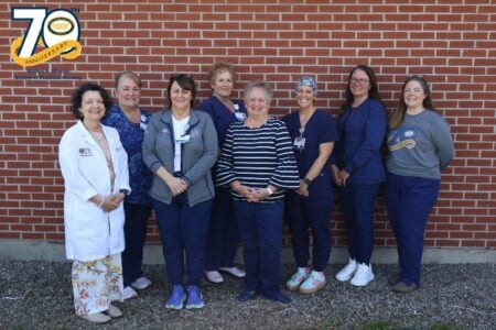 Eight staff from Marion S. Whelan School of Practical Nursing pose outdoors against a brick wall for their 70th anniversary.