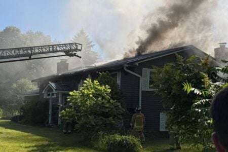 Marion firefighters battle a house fire with thick smoke billowing from the roof as a ladder truck sprays water.