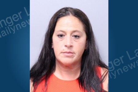 Mugshot of a woman with long dark hair and an orange top, looking forward.