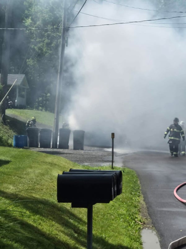 Firefighters battle a blaze producing heavy smoke on a residential street with multiple mailboxes in the foreground.