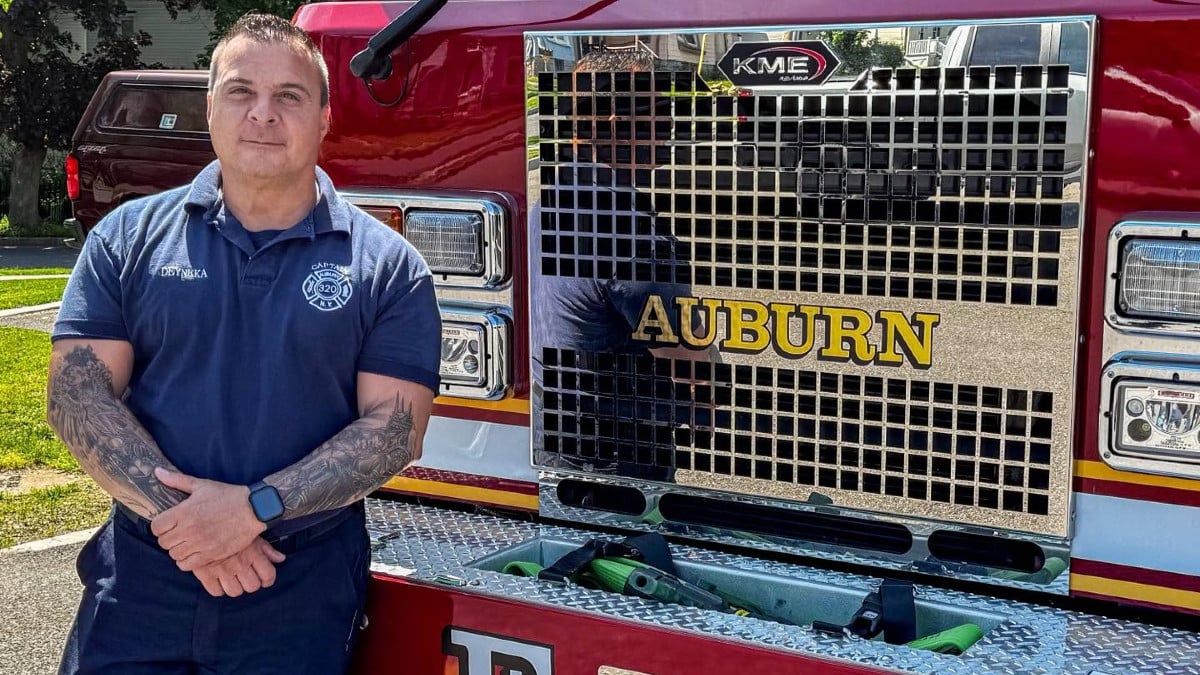 Auburn Fire Captain Deyneka stands with tattooed arms crossed in front of a red Auburn fire truck.