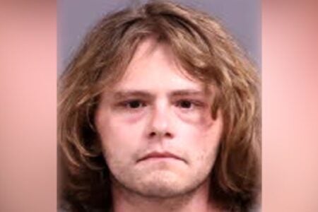 Young white man with long brown hair looks straight ahead in a police mugshot.