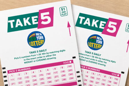 Two New York Lottery Take 5 play slips, featuring the logo and game instructions, on a light wood surface.